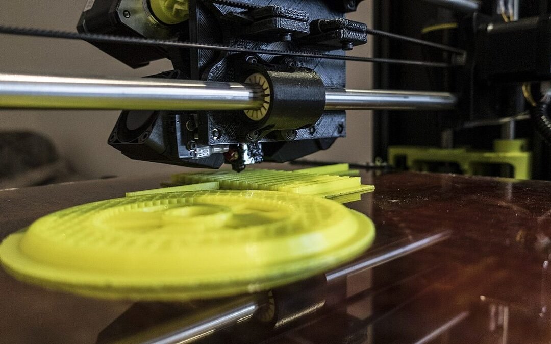 Głowica drukarki 3D nad żółtym, pierścieniowym wydrukiem na szklanym stole